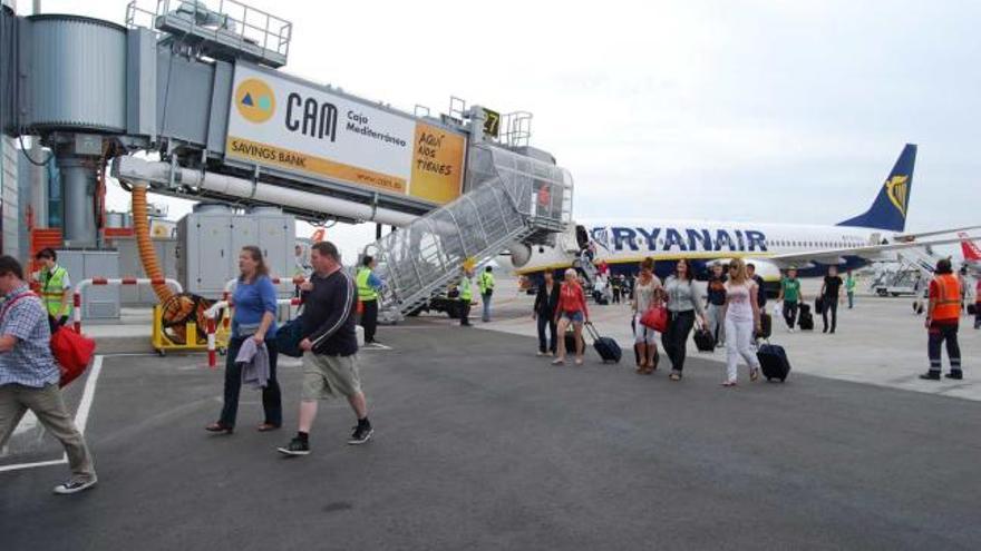 Un grupo de turistas extranjeros pasan junto a un pasarela telescópica tras desembarcar a pie de un avión de Ryanair en El Altet.