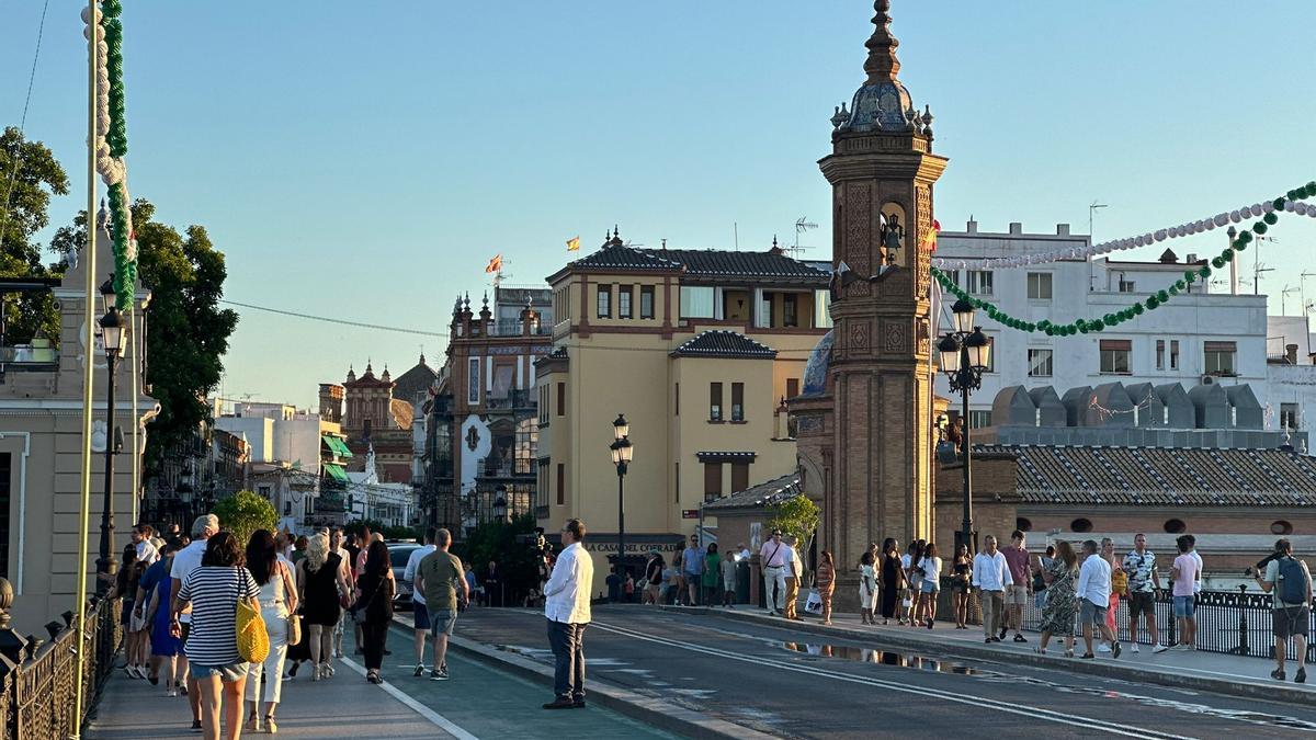 Gente camina por el puente de Triana dirección a la Velá de Santa Ana