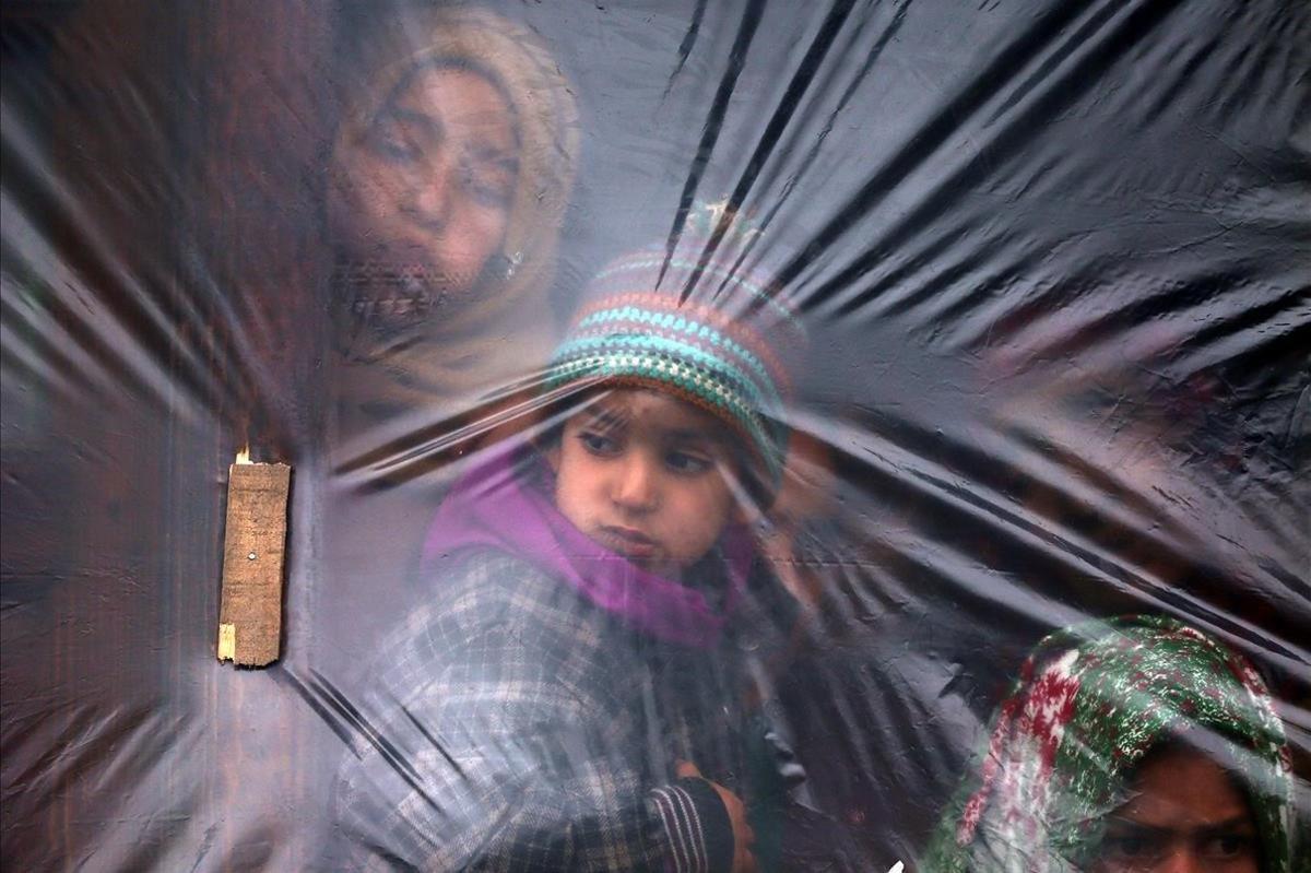 Niños mirando a través de la ventana cubierta con plástico para protegerse del frío en el sur de Cachemira.