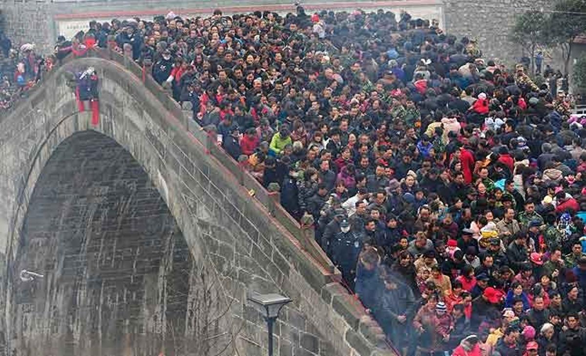 Diverses persones travessen el pont Tai Ping participant d’un esdeveniment tradicional que consisteix a llançar roba vella i monedes a l’aigua per buscar felicitat i salut a Jushui (Xina)