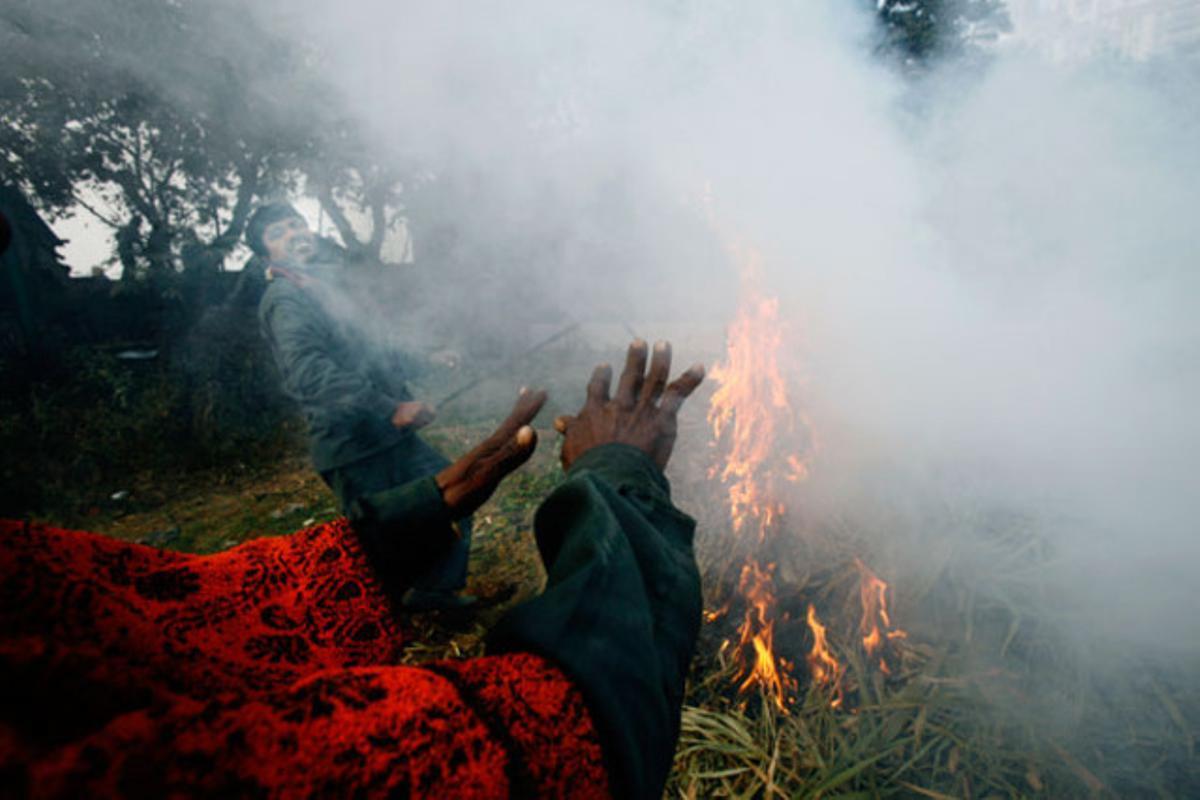 Un home s’escalfa al costat d’una foguera en una fred matí a Gurgaon (Índia).