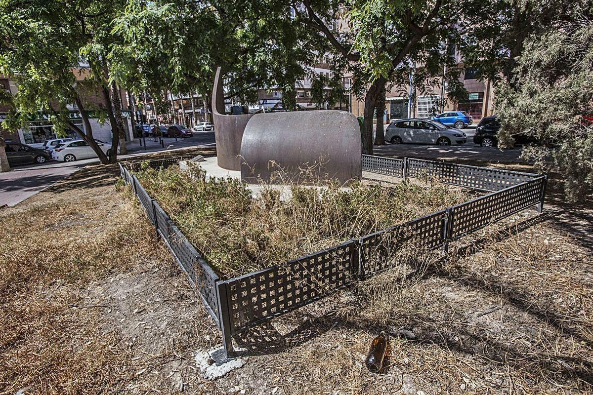 La escultura en homenaje a Miguel Hernández, en los juzgados de Benalúa, rodeada de vegetación seca.