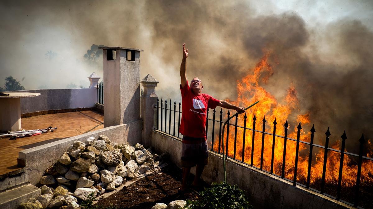 Un hombre tira agua sobre las llamas durante un incendio forestal en Canecas, en las afueras de Lisboa, Portugal, 10 de julio de 2022.