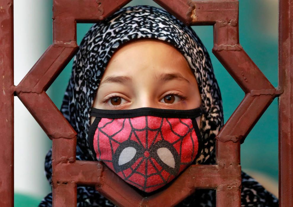 A Kashmiri girl wearing a mask looks on at the ...