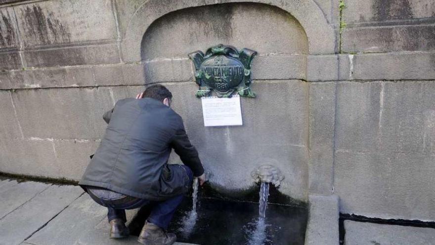 Una persona recoge agua en As Burgas, con el cartel de no apta para beber. // Noé Parga