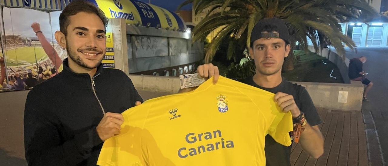 Dos aficionados de la UD junto a las taquillas del Gran Canaria, posan con las entradas y una elástica de Viera.
