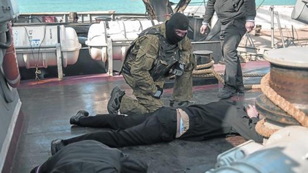 Un militar enmascarado reduce a dos hombre en un barco de guerra ucraniano.