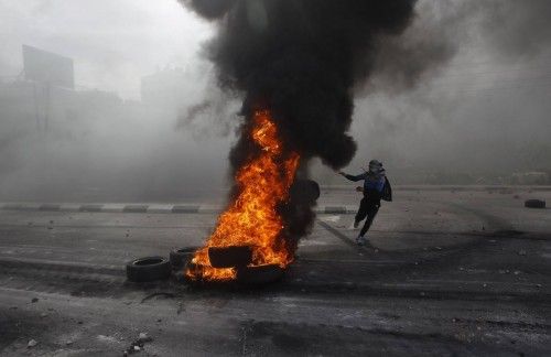 Un manifestante palestino tira un neumático al fuego durante los enfrentamientos con soldados israelíes