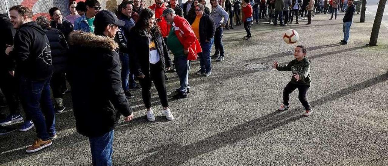 Los aficionados del Sporting hacen cola en El Molinón, con un niño jugando al balón mientras espera.