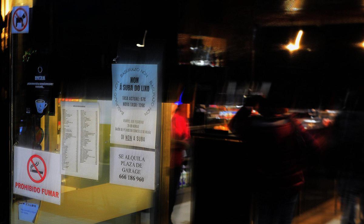 El cartel -en la foto en la cristalera de un bar- fue colgado también en el tablón de anuncios del Concello.