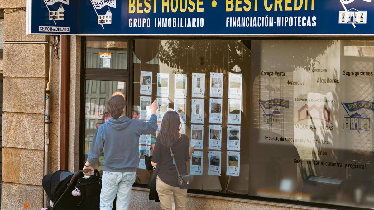 Una pareja consulta precios de viviendas en el escaparate de una inmobiliaria de Santiago