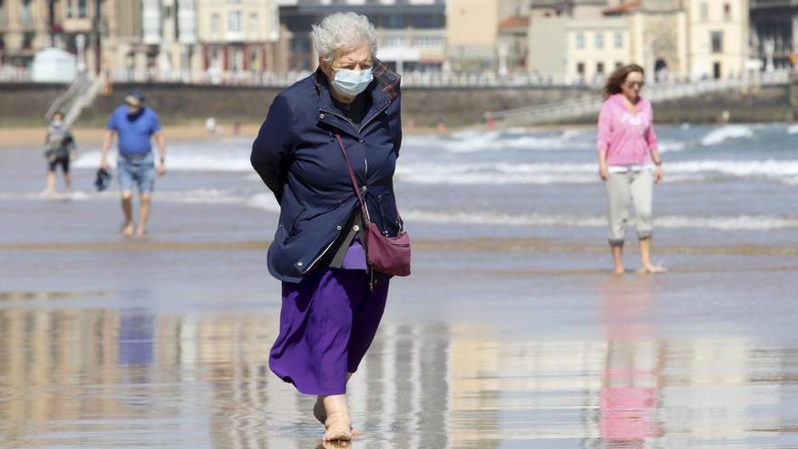 Una mujer pasea por la playa de San Lorenzo con mascarilla.
