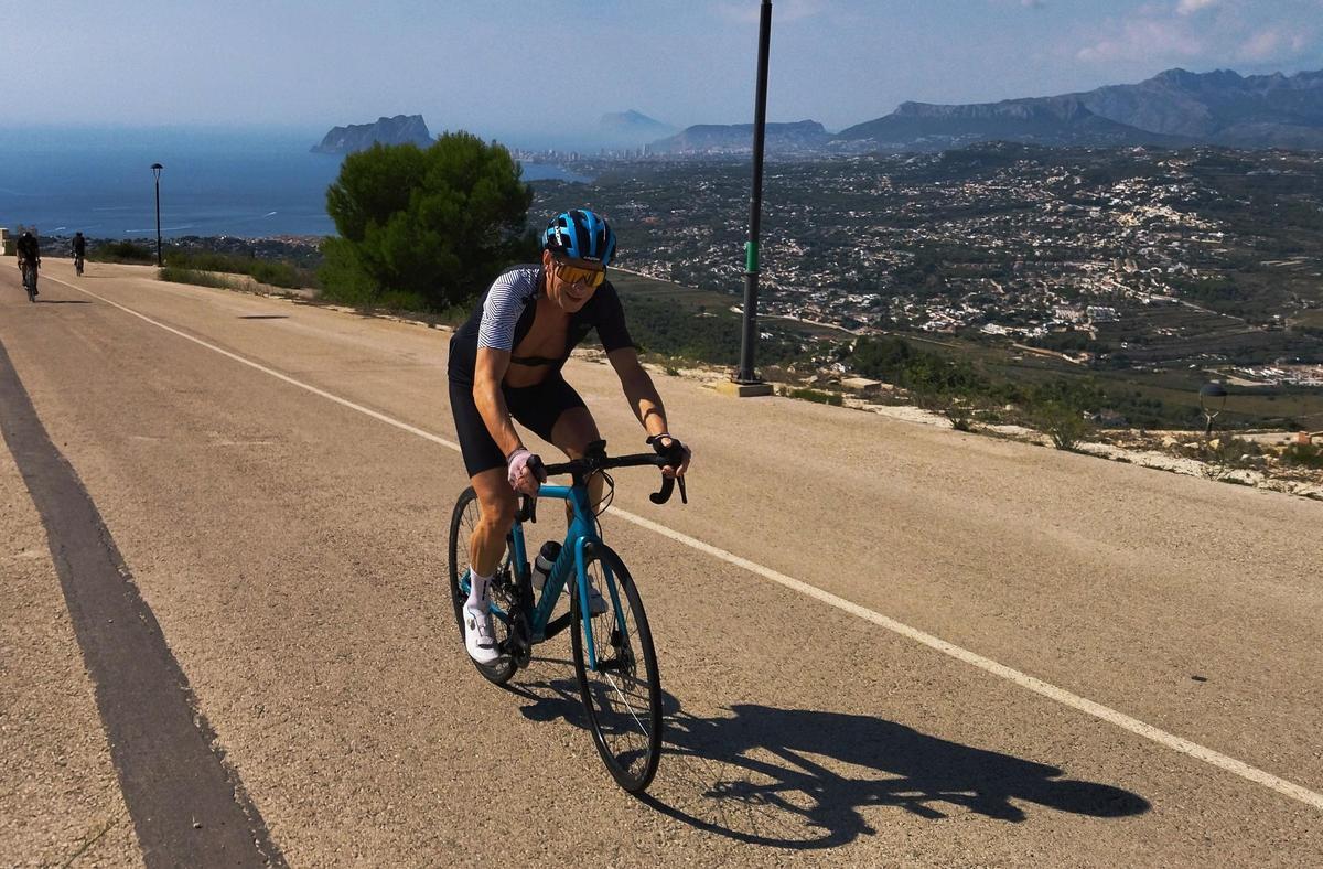 Un ciclista asciende un puerto de la Marina Alta; al fondo, el Penyal d'Ifac