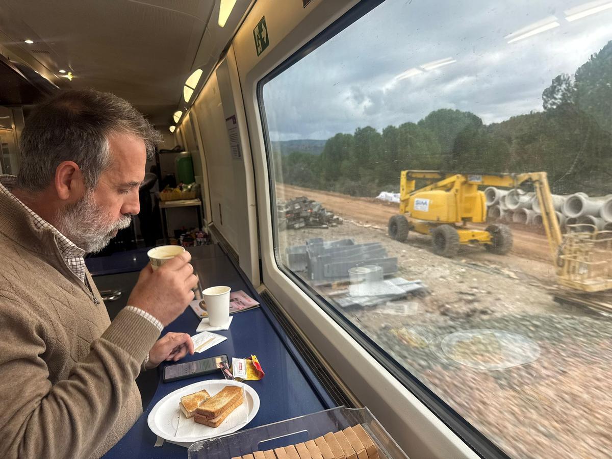 Un viajero toma su desayuno en un tren AVE entre Córdoba y Madrid, este martes por la mañana, mientras observa una máquina trabajando junto a las vías.