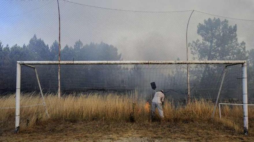 Una persona intenta apagar las llamas del fuego que se originó en la parroquia ourensana de Palmés.