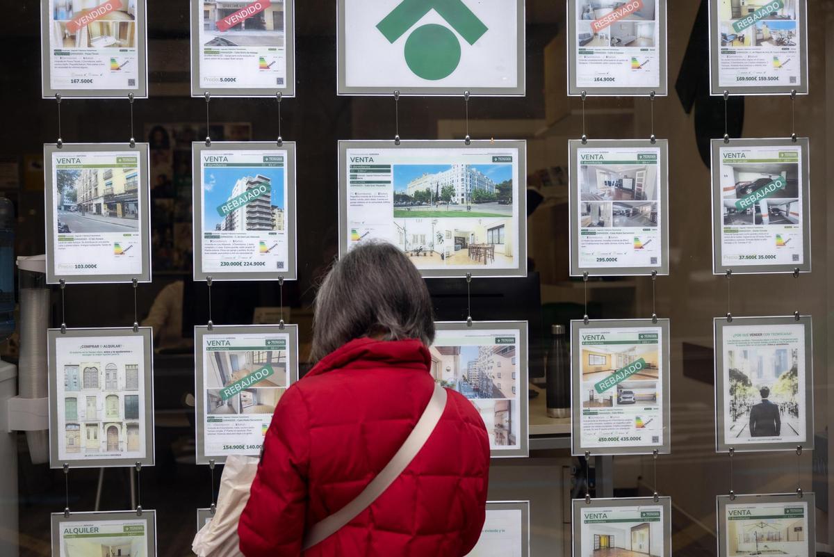 Una mujer consulta los anuncios de vivienda en el escaparate de una agencia inmobiliaria situada en una calle de la ciudad de Zaragoza.