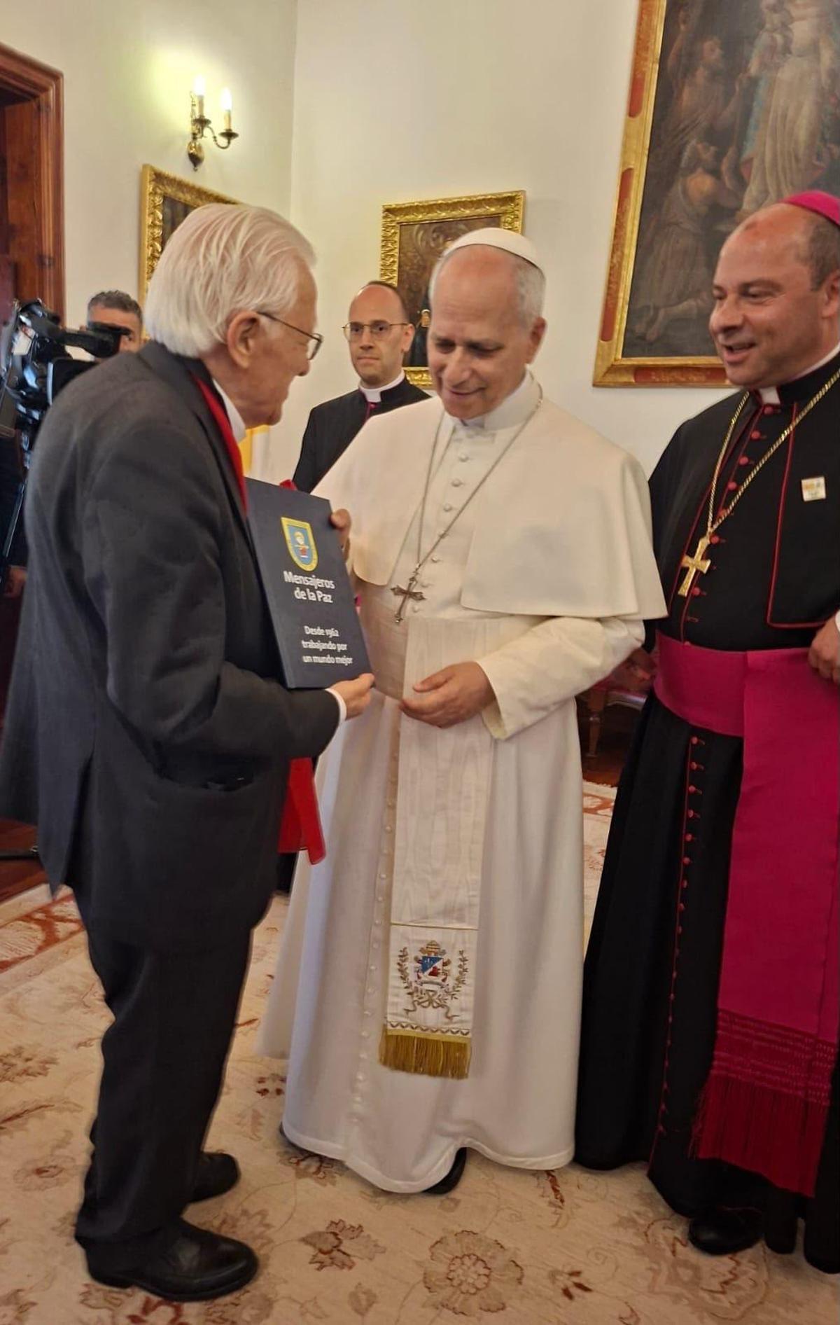 El padre Ángel, de espaldas, entrega a León XIV la memoria de Mensajeros de la Paz, en Tenerife.