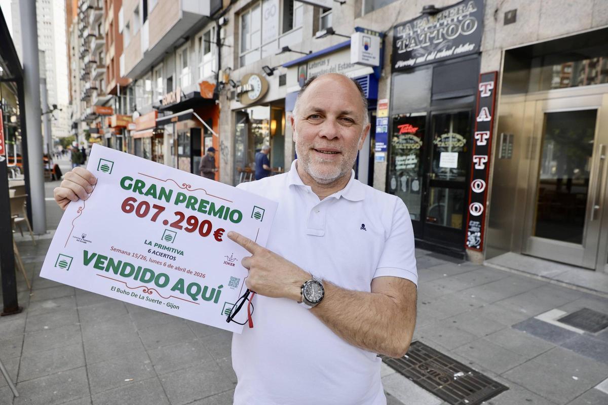 Borja Muñiz, de "El Búho de la Suerte," posando este martes con el cartel acreditativo del reparto del premio frente a su local, en la Acerona.