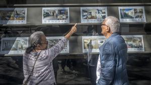 Dos personas miran carteles de pisos de alquiler y compra en una inmobiliaria de Barcelona.