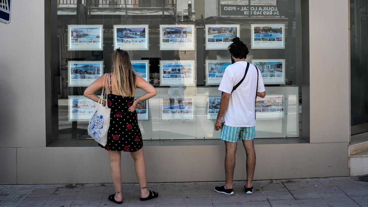 Eine Frau und ein Mann schauen sich Immobilienangebote im Aushang eines Maklerbüros in Palma de Mallorca an.