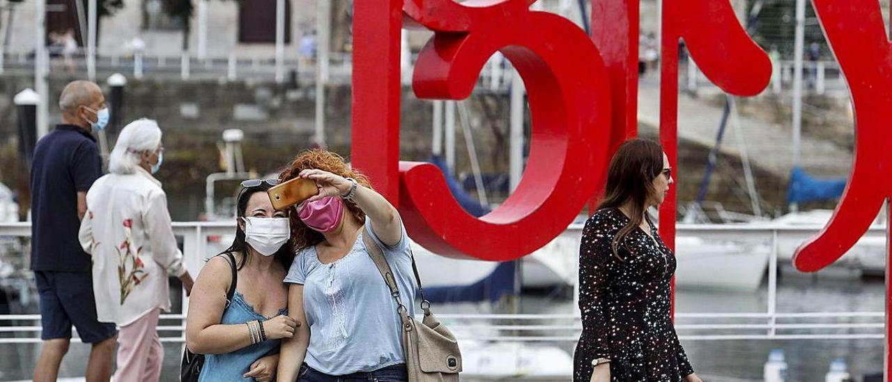 Unas turistas con mascarilla se hacen una foto delante de las &quot;letronas&quot; de Gijón.