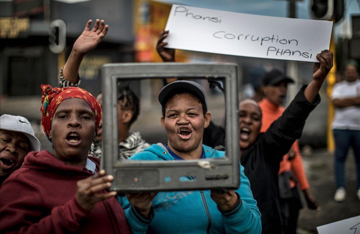 Una mujer sostiene una pancarta contra la corrupción, mientras las demás gritan consignas contra la falta de prestación de servicios o necesidades básicas como el acceso al agua y la electricidad en Johannesburgo.