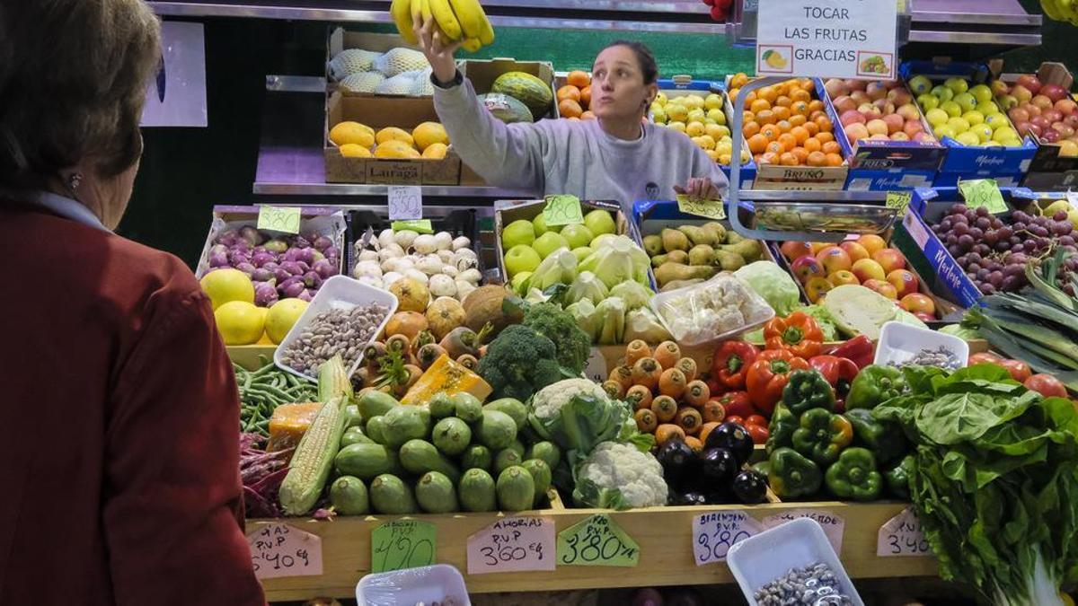 Una mujer es atendida por la tendera en un puesto de frutas y verduras.