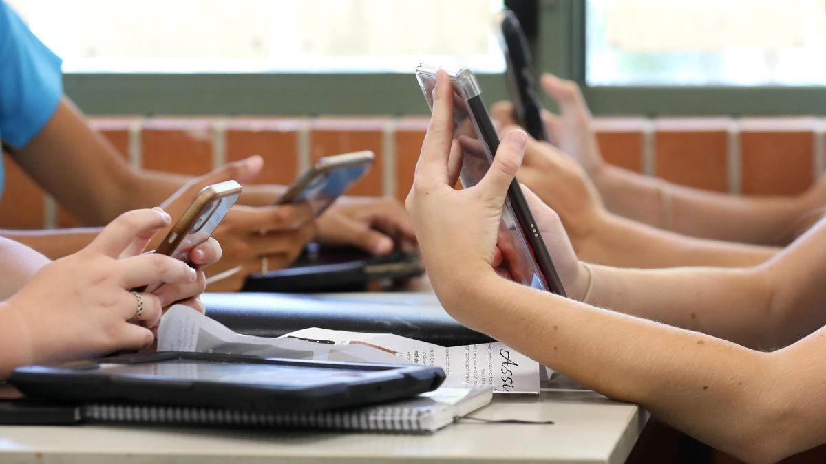 Menores usando sus teléfonos móviles en un centro escolar.