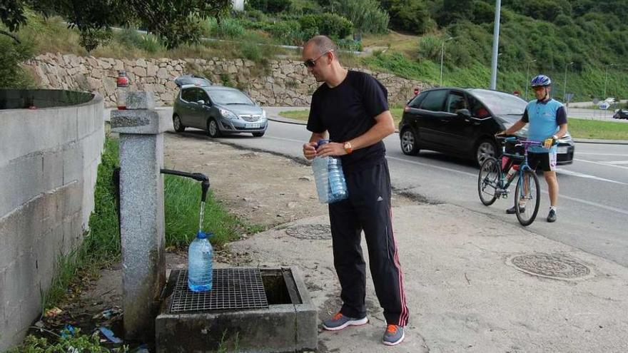 Una persona recoge agua en una fuente en la rotonda de Cabanas, en la parroquia de Trasmañó. // Faro