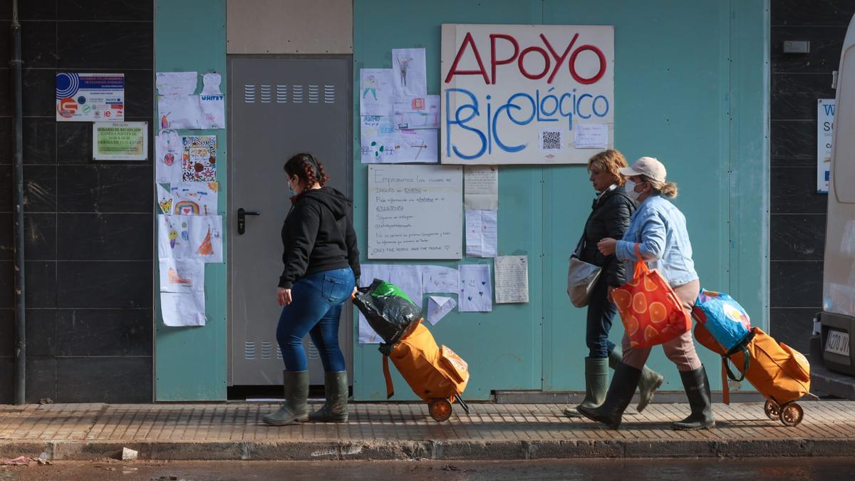 Unas mujeres pasan por delante de un cartel de apoyo psicológico en Paiporta.