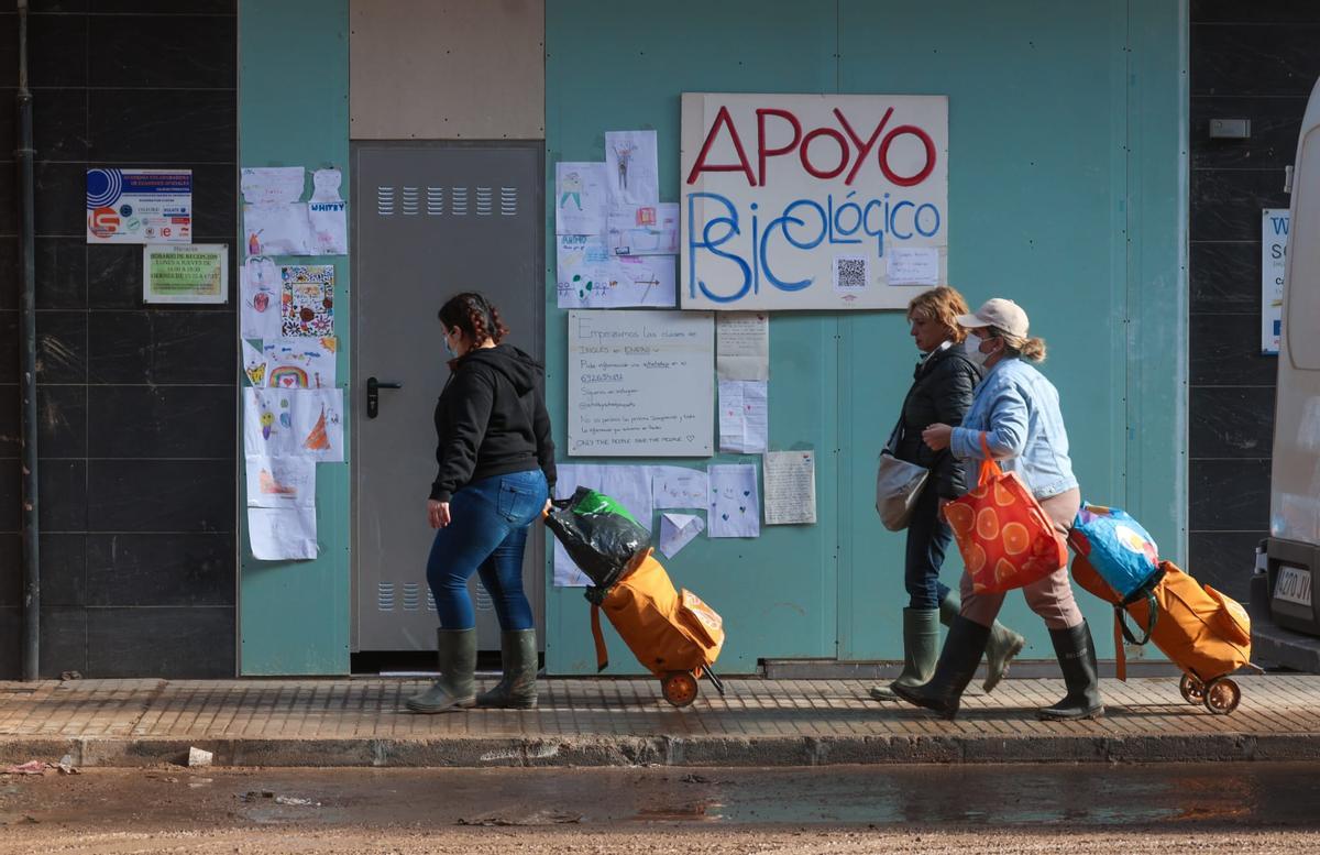Unas mujeres pasan por delante de un cartel de apoyo psicológico en Paiporta.
