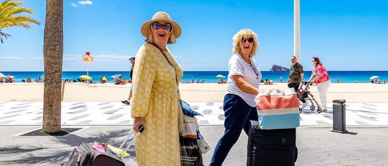 Dos turistas británica caminan equipaje en mano por el paseo de la playa de Levante de Benidorm