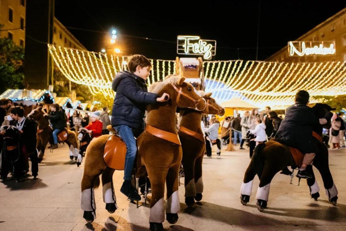 Unos niños pasean en pony eléctrico en la Muestra Navideña de la Plaza del Pilar