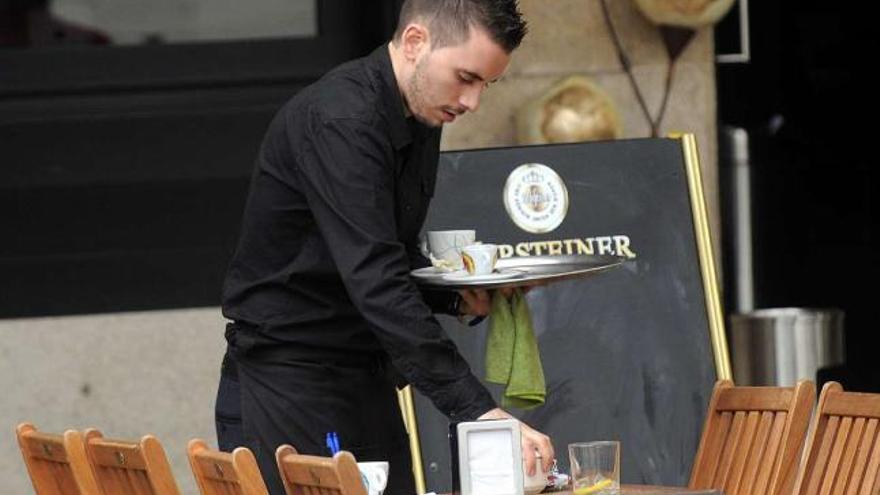 Un camarero recoge una mesa de la terraza de un bar.  // Rafa Vázquez