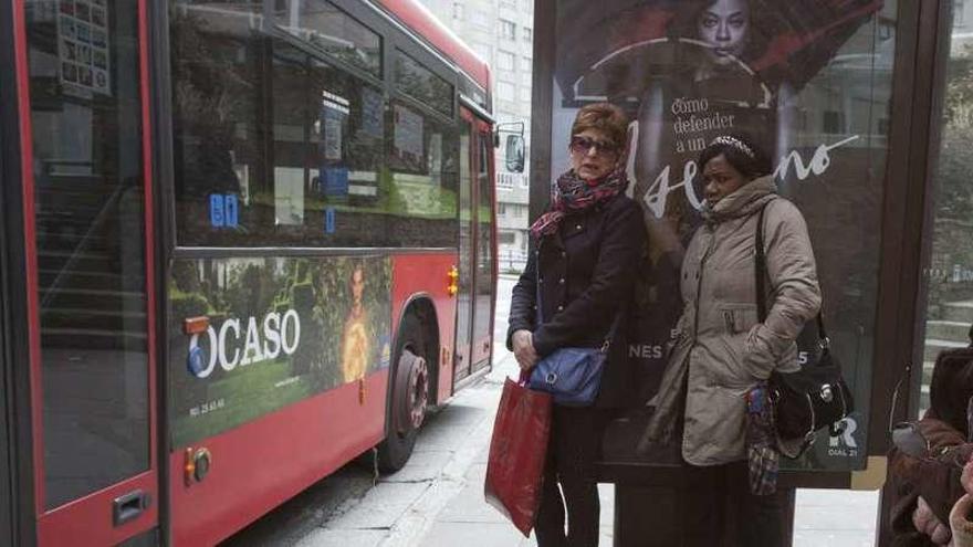 Usuarios de Tranvías esperan en una marquesina, ante un bus urbano.