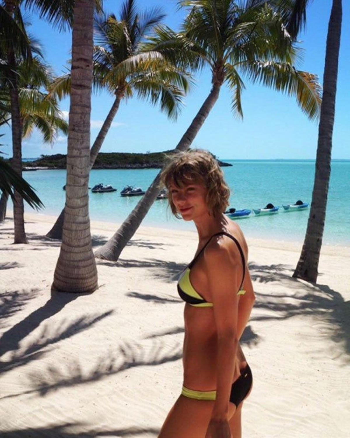 Taylor Swift camina por la playa cerca de las palmeras.