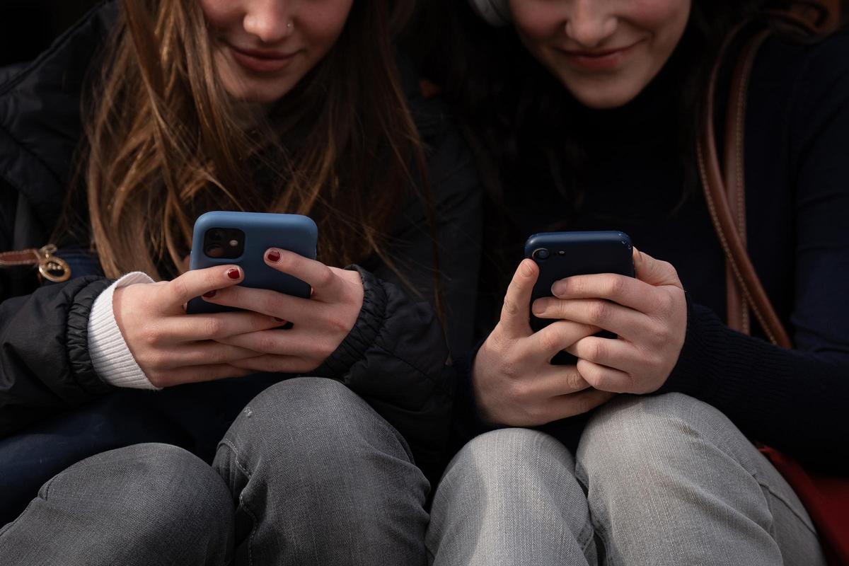 Dos chicas jóvenes consultan sus teléfonos móviles.