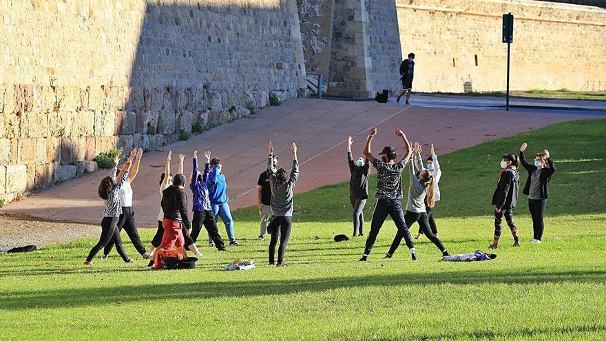 Un grupo de personas realizan ejercicio y estiramientos por la mañana, a pleno sol, en la Muralla de Cartagena.