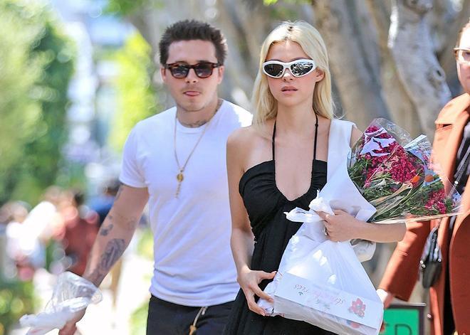 Nicola Peltz con vestido negro escote cruzado acompañada por Brooklyn Beckham