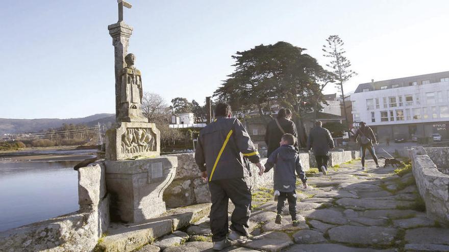 Viandantes junto al cruceiro de San Telmo roto, ayer, en el puente medieval de A Ramallosa. // Adrián Irago