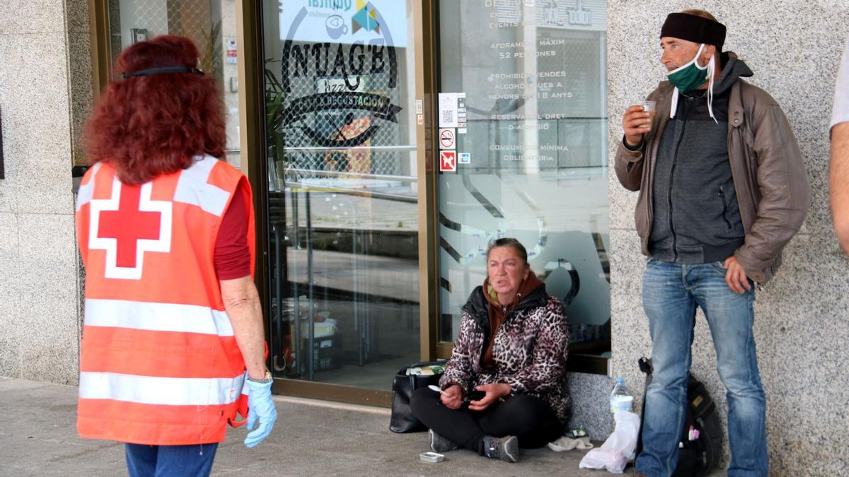 Una trabajadora de la Cruz Roja atiende a dos personas en la calle.