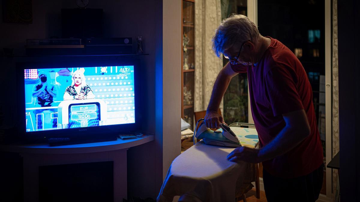 Un hombre plancha mientras ve la televisión.