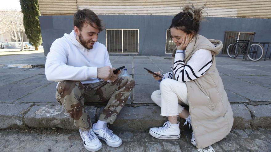 Dos jóvenes observan sus teléfonos móviles mientras conversan entre ellos.