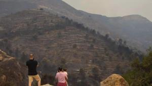 Una familia observa el devastado paisaje que ha dejado el incendio.