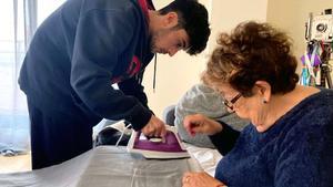 Un joven plancha una cortina en casa, con su abuela.