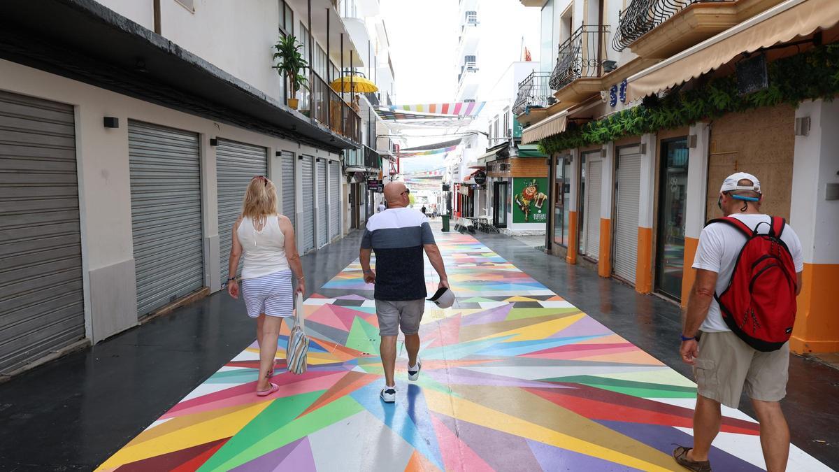 Varios turistas pasean por la calle principal del West End sobre la obra de Okuda.