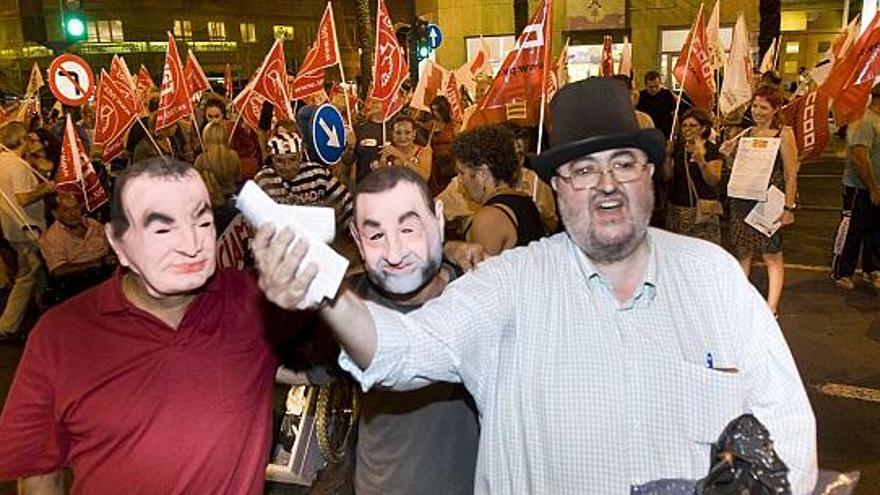 Varios manifestantes realizan una parodia en la que un hombre reparte billetes ante la sede de las oficinas de Enrique Ortiz.