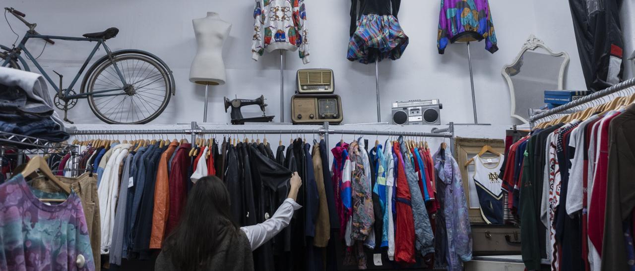 Una mujer mira ropa vintage de segunda mano en la tienda La Vespa Roja, de València.