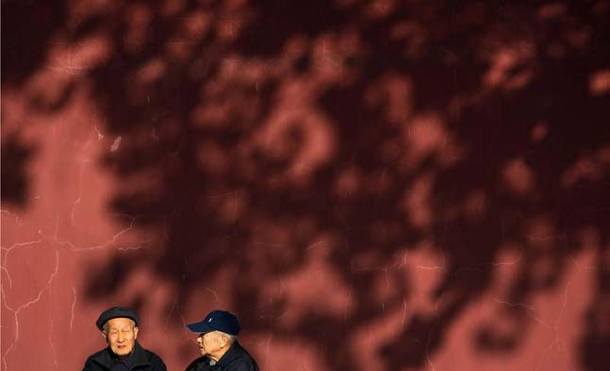 Dos ancianos hablan delante de una pared roja, cerca de la Plaza de Tiananmen (Pekín).