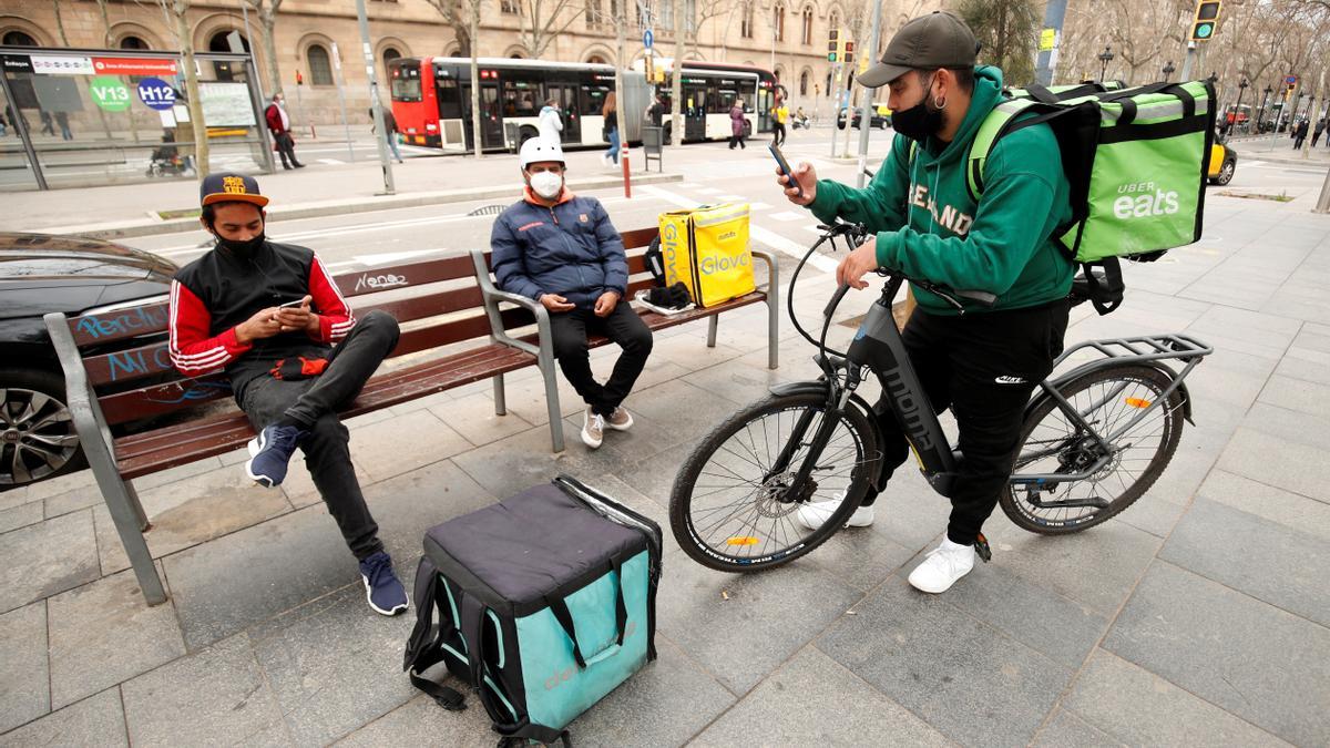 Delivery riders with backpacks of Glovo, Uber eats and Deliveroo wait for orders at Universitat square in Barcelona